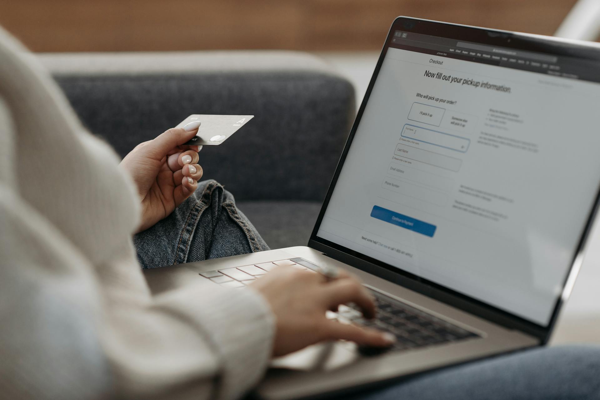 Person holding a credit card and typing on a laptop, completing an online checkout form for order pickup.